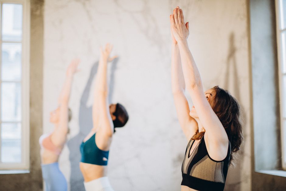 A warm, light-filled yoga studio with wooden floors and soft morning light streaming through large windows
